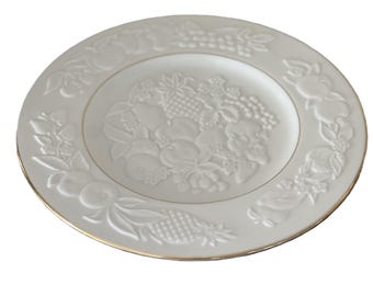 Könnte beinhalten: Weiße Keramikplatte mit geprägtem Obstdesign, darunter Trauben, Äpfel und Birnen. Die Platte hat einen goldenen Rand. Ein dekoratives Stück zum Servieren oder Ausstellen, ca. 25 cm im Durchmesser.
