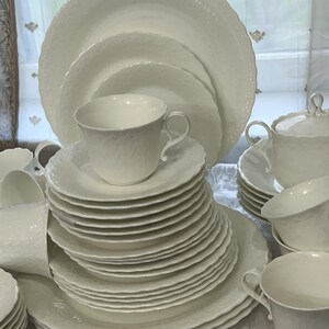 May include: A set of white porcelain tableware, featuring plates, teacups, saucers, and a lidded serving dish. The items have a textured finish and a scalloped edge, offering a refined and traditional appearance.