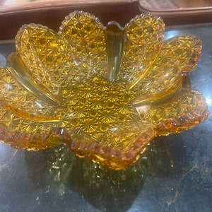 May include: A vintage amber glass bowl with a scalloped edge and a starburst pattern. The bowl is made of pressed glass and has a delicate, feminine design.