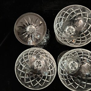 May include: Four clear glass wine glasses with a cut crystal design. The glasses are arranged in a circle on a black surface.