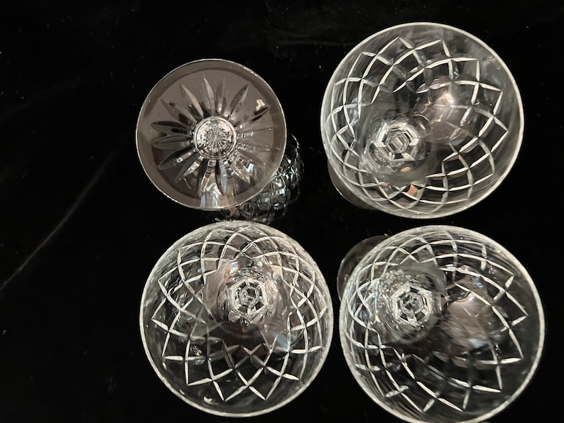 May include: Four clear glass wine glasses with a cut crystal design. The glasses are arranged in a circle on a black surface.