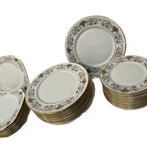 May include: A collection of white porcelain plates with a gold rim and floral pattern. The plates are in various shapes and sizes, including round and oval. The floral design includes pink, yellow, and green accents. A classic dinnerware set.