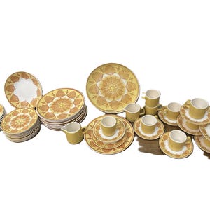 Puede incluir: Un juego de vajilla vintage completo en amarillo y blanco, con platos, cuencos, tazas, platillos y una jarra de crema. Los platos y cuencos tienen un patrón floral decorativo en tonos amarillos y marrones.