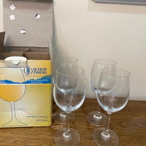 K&ouml;nnte beinhalten: Vier klare Weingl&auml;ser aus Glas mit einer Schachtel Schott Zwiesel Connoisseur's Crystal Lexington Collection Wei&szlig;wein im Hintergrund.
