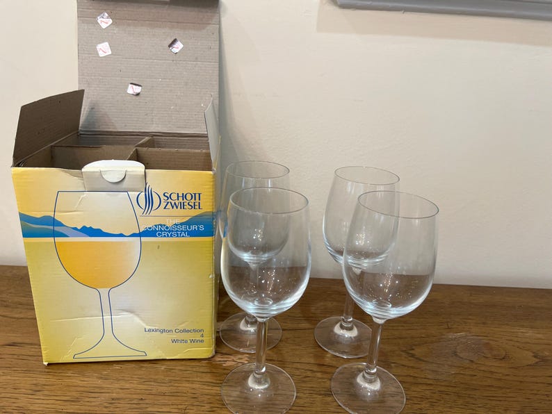 K&ouml;nnte beinhalten: Vier klare Weingl&auml;ser aus Glas mit einer Schachtel Schott Zwiesel Connoisseur's Crystal Lexington Collection Wei&szlig;wein im Hintergrund.