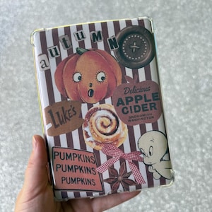 May include: A clear phone case with a fall-themed design. The case features a pumpkin, cinnamon roll, and the text "Delicious Apple Cider" and "Pumpkins". The design has a striped background and a cartoon ghost.
