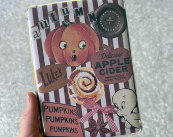 May include: A clear phone case with a fall-themed design. The case features a pumpkin, cinnamon roll, and the text "Delicious Apple Cider" and "Pumpkins". The design has a striped background and a cartoon ghost.