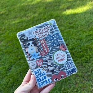 May include: Clear Kindle case with a zebra print background and various stickers. Stickers include "Emotional Support Kindle", "Hot Girls Read Books", a dog, and the text "Can I have your pickle?"
