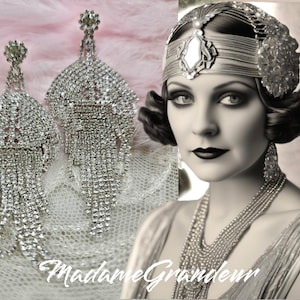 May include: A pair of silver crystal chandelier earrings with a teardrop shape. The earrings are made of many small crystals that dangle from a central point. The earrings are shown on a white background.