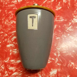MCM style ceramic two-tone tea caddy, grey glazed with stencilled "T" and blonde wood lid with retro metal knob, circa 2000s.