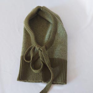 May include: Olive green knit balaclava with a ribbed bottom and a drawstring closure. The balaclava is made of a soft, textured knit material. The hood is designed to cover the head and neck.