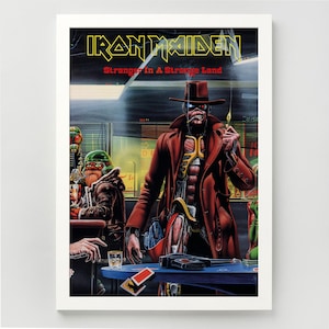 May include: A framed poster featuring the Iron Maiden Stranger In A Strange Land artwork. It depicts a cyborg figure in a brown trench coat and hat holding a lit match in a dimly lit bar setting with other characters, a handgun, and a glass.