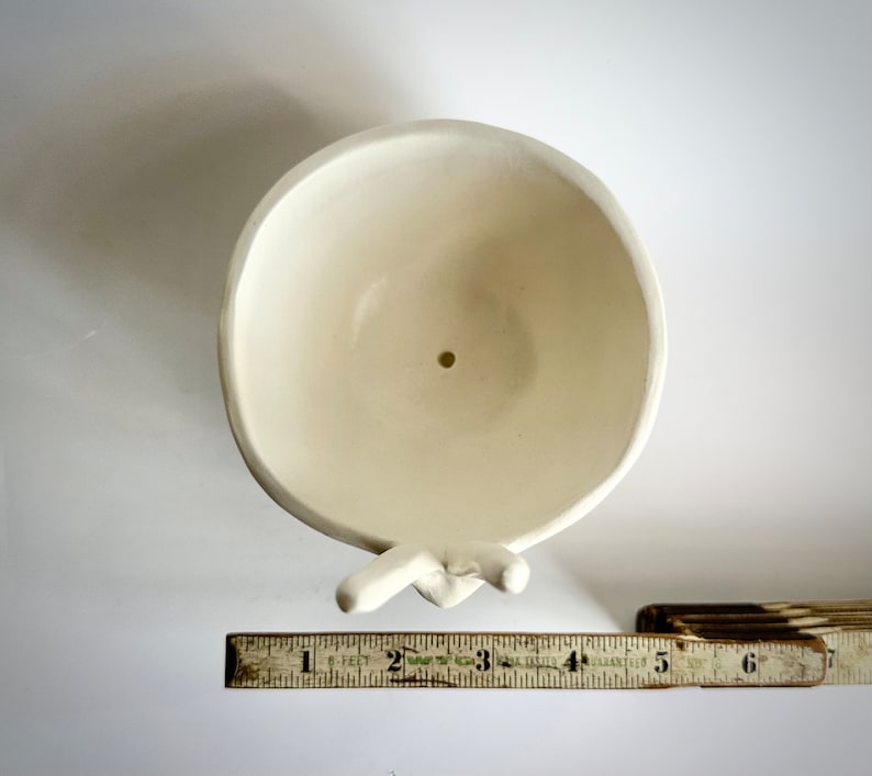 May include: White ceramic planter shaped like two hands holding a bowl. The bowl has a drainage hole in the bottom.