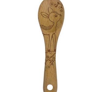 May include: Wooden cooking spoon with a deer design etched into the surface. The deer is depicted with a floral crown and is surrounded by floral and leaf accents. The spoon has a hole in the handle for hanging.