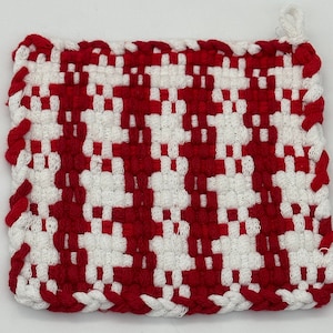 May include: Square, woven potholder in a red and white checkerboard pattern. The edges are finished with a red braided trim and a small loop for hanging. The potholder is made of a thick, durable material.