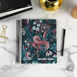 May include: A spiral-bound notebook featuring a dark teal cover with a pattern of a pink snake, moths, bats, mushrooms, crystals, and potion bottles. The name Samantha Ingram is printed in white script at the bottom right of the cover.