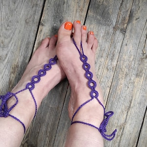 以下が含まれることがあります： 装飾的なデザインの紫色のクロシェフットジュエリー。ジュエリーは両方の足に着用され、足首にタイがあります。