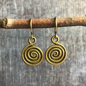 May include: A pair of gold-toned spiral earrings with a simple design. The earrings are hanging from a branch.