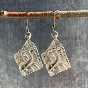 May include: A pair of silver earrings with a textured, tree-like design. The earrings are hanging from a branch.
