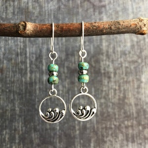 May include: Silver dangle earrings with turquoise beads and a wave design.
