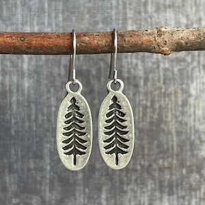 May include: A pair of silver earrings with a tree design. The earrings are oval shaped and have a silver hook.