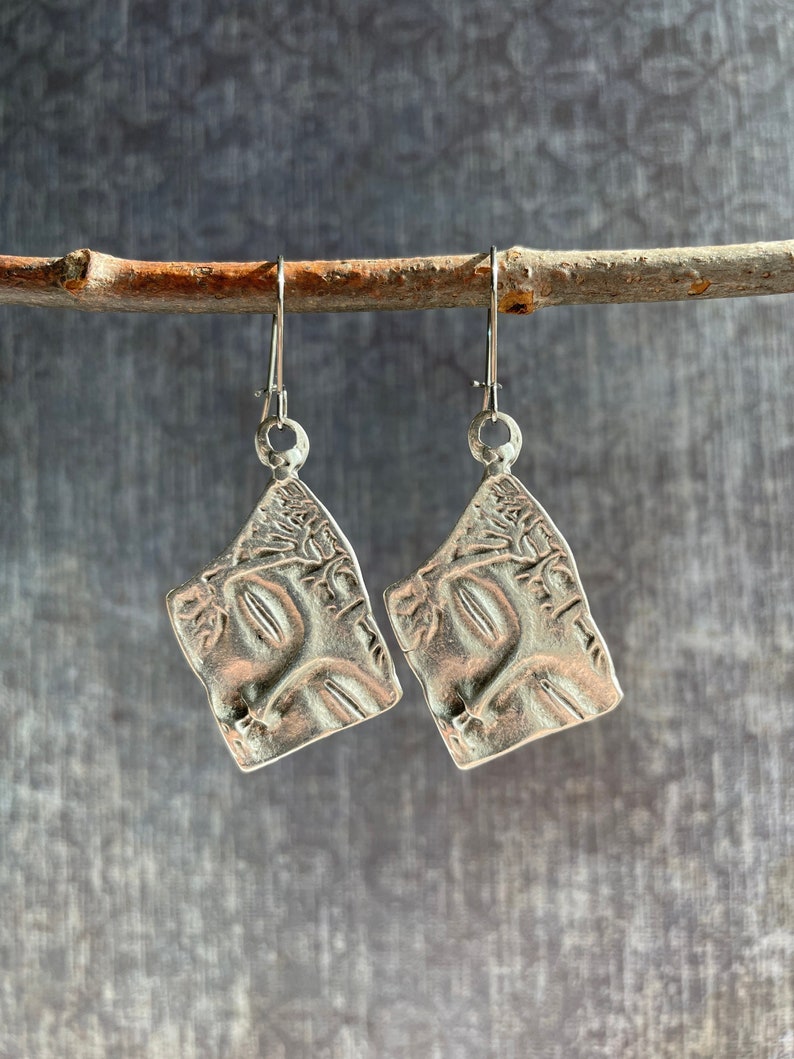 May include: A pair of silver earrings with a textured, tree-like design. The earrings are hanging from a branch.