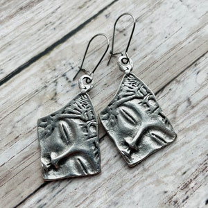 May include: A pair of silver earrings with a textured, abstract design. The earrings are made of metal and have a simple, modern style.
