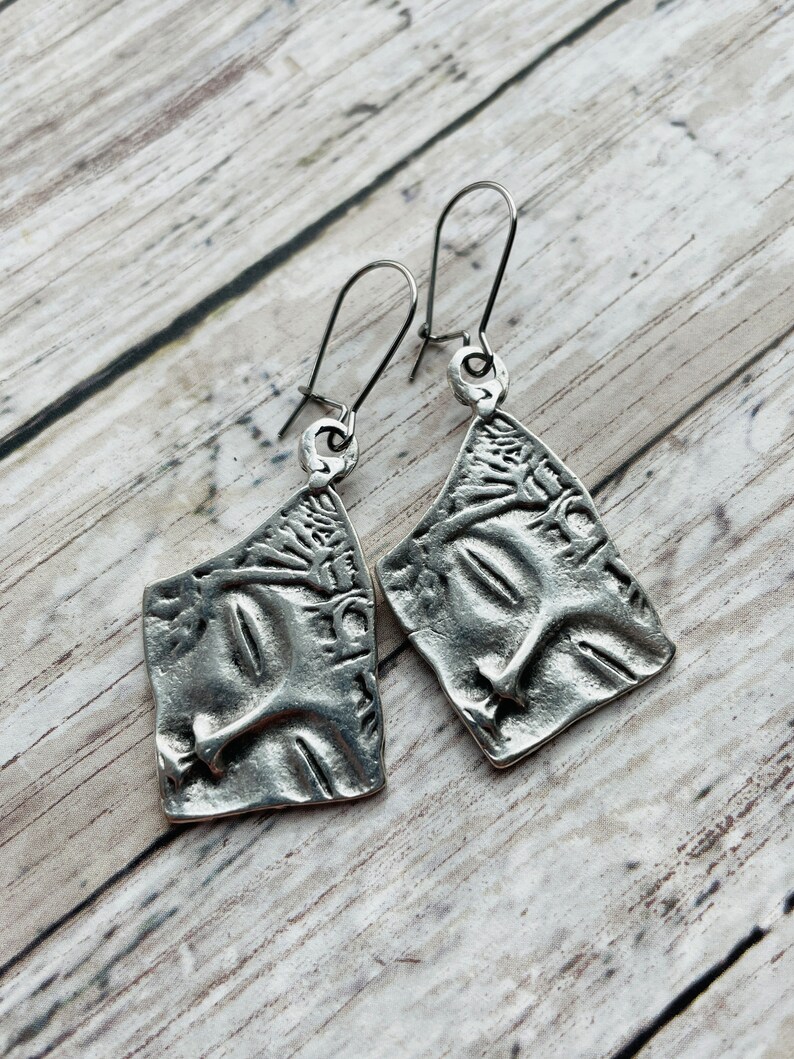 May include: A pair of silver earrings with a textured, abstract design. The earrings are made of metal and have a simple, modern style.