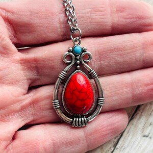 Peut inclure: Un collier en cha&icirc;ne argent avec un pendentif en pierre rouge et turquoise. Le pendentif est en forme de larme et pr&eacute;sente un design d&eacute;taill&eacute;.
