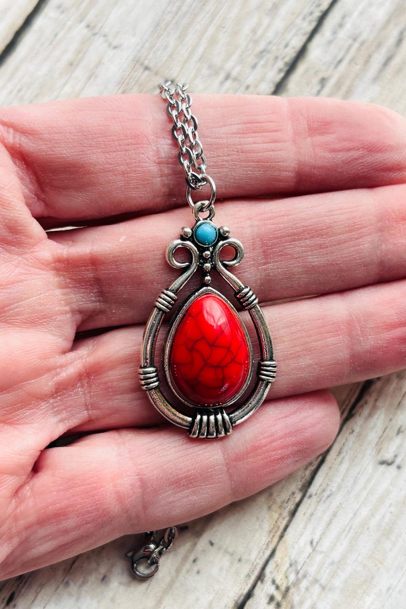 Peut inclure: Un collier en cha&icirc;ne argent avec un pendentif en pierre rouge et turquoise. Le pendentif est en forme de larme et pr&eacute;sente un design d&eacute;taill&eacute;.