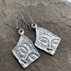 May include: A pair of silver earrings with a face design. The earrings are made of metal and have a simple, elegant design.