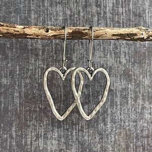 May include: Silver heart shaped dangle earrings with a hammered texture.