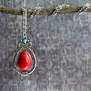 Peut inclure: Un collier en cha&icirc;ne argent avec un pendentif en pierre rouge. Le pendentif est entour&eacute; d'un cadre argent&eacute; avec un accent turquoise.