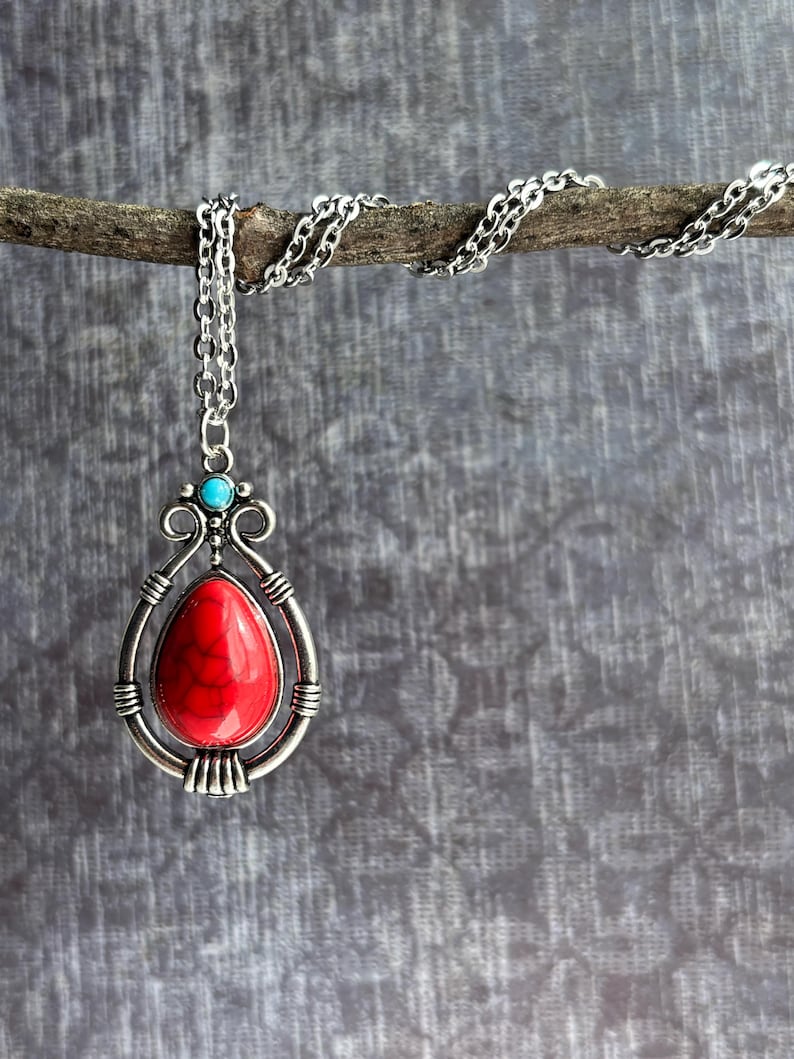 Peut inclure: Un collier en cha&icirc;ne argent avec un pendentif en pierre rouge. Le pendentif est entour&eacute; d'un cadre argent&eacute; avec un accent turquoise.