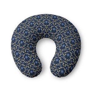 Puede incluir: Una almohada de lactancia en forma de C con un fondo azul marino oscuro y un patrón repetitivo de flores azul claro, tallos marrones delgados y pequeñas hojas de color crema dispuestas en un diseño botánico simétrico por toda la superficie.