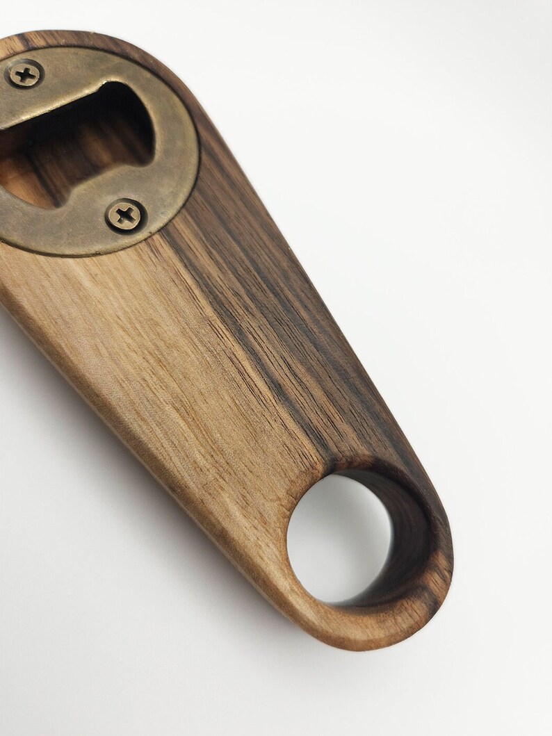 K&ouml;nnte beinhalten: Ein Flaschen&ouml;ffner aus Holz mit einem Messing-Oberteil und einem Ringgriff. Das Holz hat ein dunkelbraunes und hellbraunes Streifenmuster.