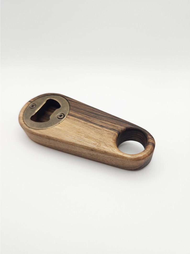 K&ouml;nnte beinhalten: Ein Flaschen&ouml;ffner aus Holz mit einem Messing-Kronkorken&ouml;ffner. Der &Ouml;ffner hat einen Ring am Ende zum einfachen Aufh&auml;ngen.
