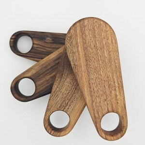 K&ouml;nnte beinhalten: Drei Holz-Servierl&ouml;ffel mit abgerundeter ovaler Form und einem Loch im Griff. Die L&ouml;ffel sind aus dunkelbraunem Holz mit nat&uuml;rlicher Maserung.