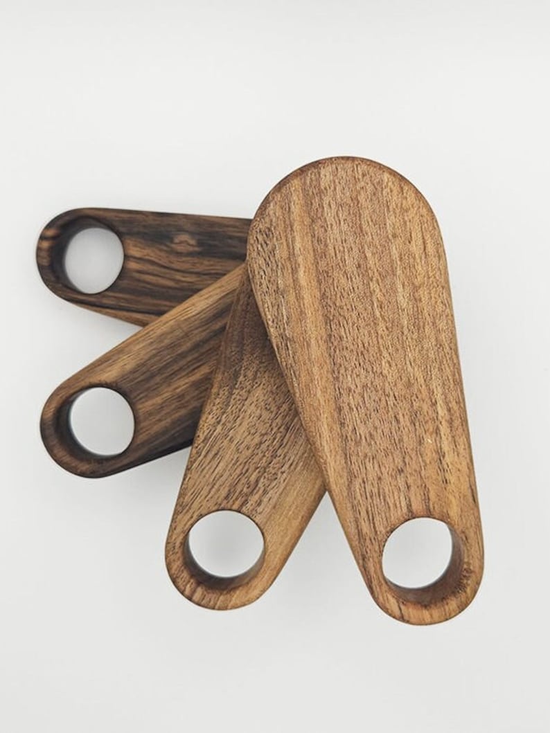 K&ouml;nnte beinhalten: Drei Holz-Servierl&ouml;ffel mit abgerundeter ovaler Form und einem Loch im Griff. Die L&ouml;ffel sind aus dunkelbraunem Holz mit nat&uuml;rlicher Maserung.