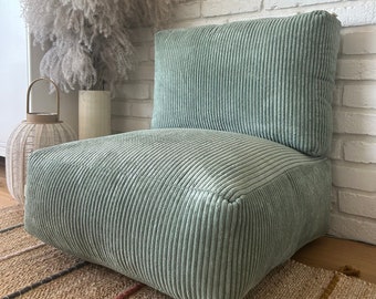 May include: A light green corduroy floor cushion with a square shape. The cushion is sitting on a woven rug with brown, red, and yellow stripes.