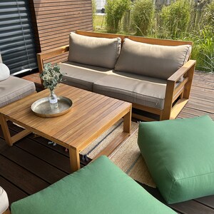 May include: A wooden outdoor sofa with beige cushions, a wooden coffee table, and two green poufs on a wooden deck.