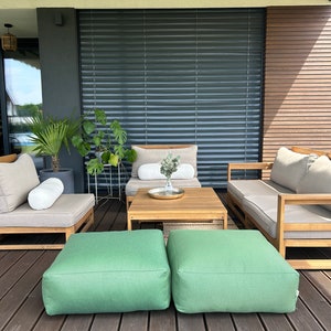May include: A wooden patio furniture set with two green ottomans, a wooden coffee table, and two beige lounge chairs with white cushions. The furniture is on a wooden deck.