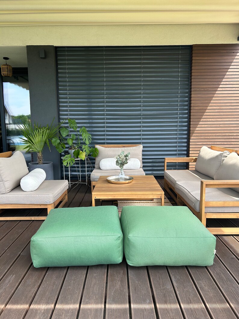 May include: A wooden patio furniture set with two green ottomans, a wooden coffee table, and two beige lounge chairs with white cushions. The furniture is on a wooden deck.