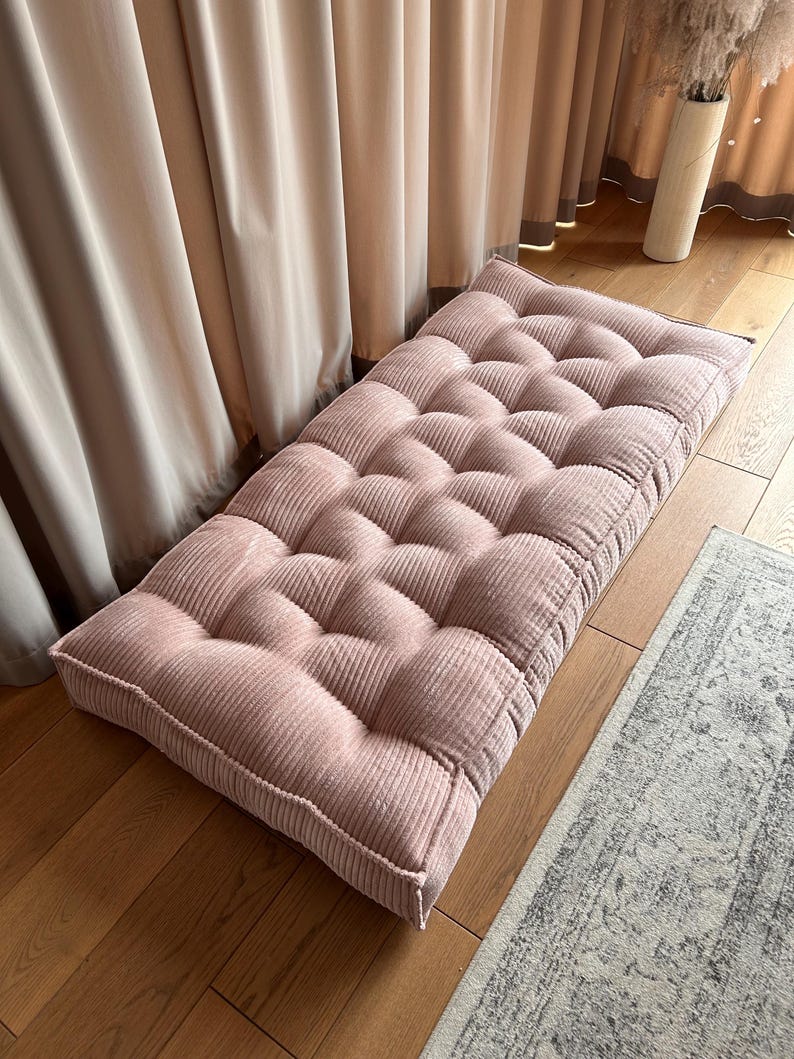 May include: A pink corduroy floor cushion with a tufted design. The cushion is rectangular and has a thick, padded base.