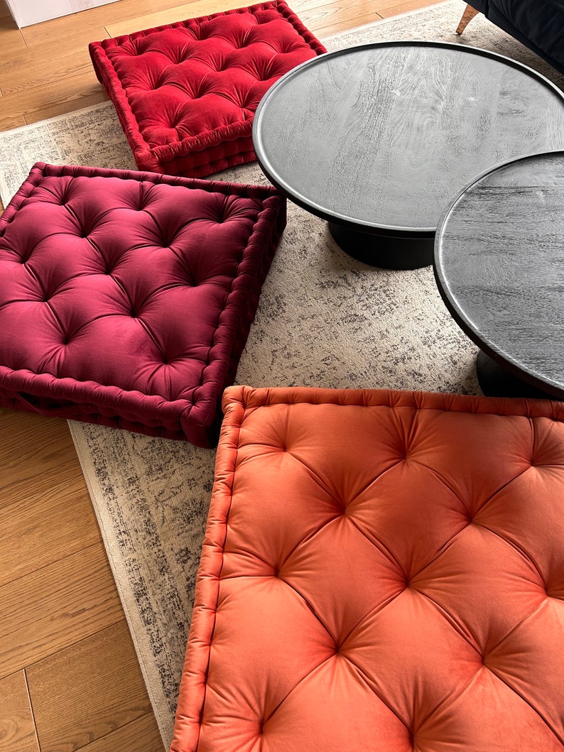 May include: Three square floor cushions with tufted tops. Two cushions are burgundy velvet and one is a burnt orange velvet.