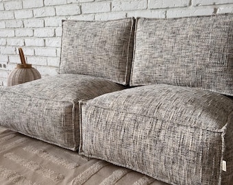 May include: A gray and white patterned modular sofa made of multiple cushions. The sofa is made of a soft, textured fabric.