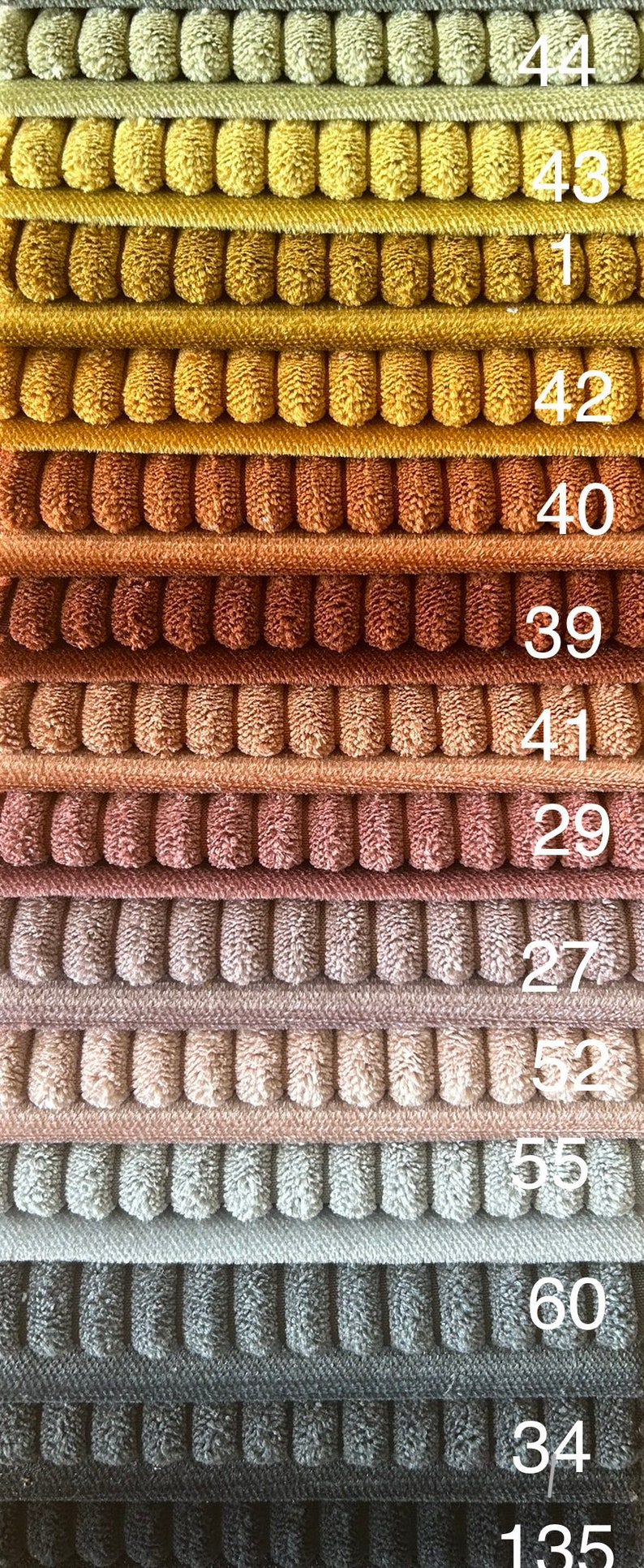 Op de afbeelding: Een stapel van 11 stofstalen in verschillende tinten bruin, beige, grijs en roze. De stalen zijn genummerd 44, 43, 41, 42, 40, 39, 41, 29, 27, 52, 55, 60, 34 en 135.