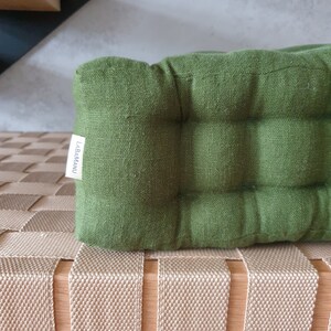 Op de afbeelding: Een groen linnen kussen met een label met de tekst "LABAMAU" op een beige geweven bank.