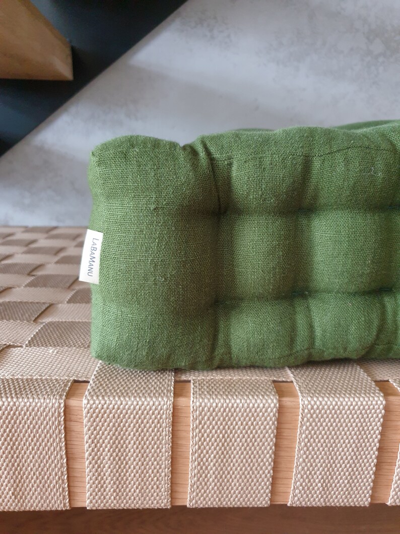 Op de afbeelding: Een groen linnen kussen met een label met de tekst "LABAMAU" op een beige geweven bank.