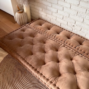 May include: A brown tufted floor cushion with a button-tufted design. The cushion is made of a soft, plush fabric and is perfect for adding a touch of comfort and style to any room.